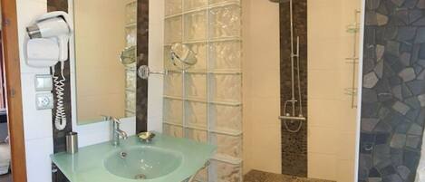 A bathroom with a glass sink, a hairdryer, a shower, and a tiled floor.