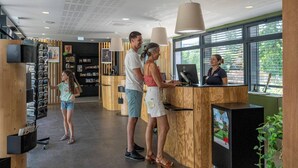 Una zona de recepción con mostradores de madera, una pantalla digital y un ventanal con vistas a zonas verdes.