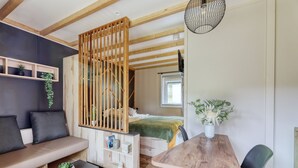Una habitación acogedora con techo de madera, una cama con manta verde, una mesa de madera, un banco y un televisor en la pared.