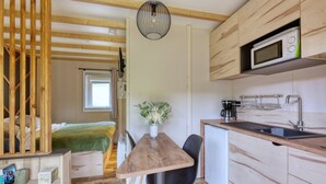 Una cocina compacta con una mesa de madera, sillas negras, un microondas y un lavabo.