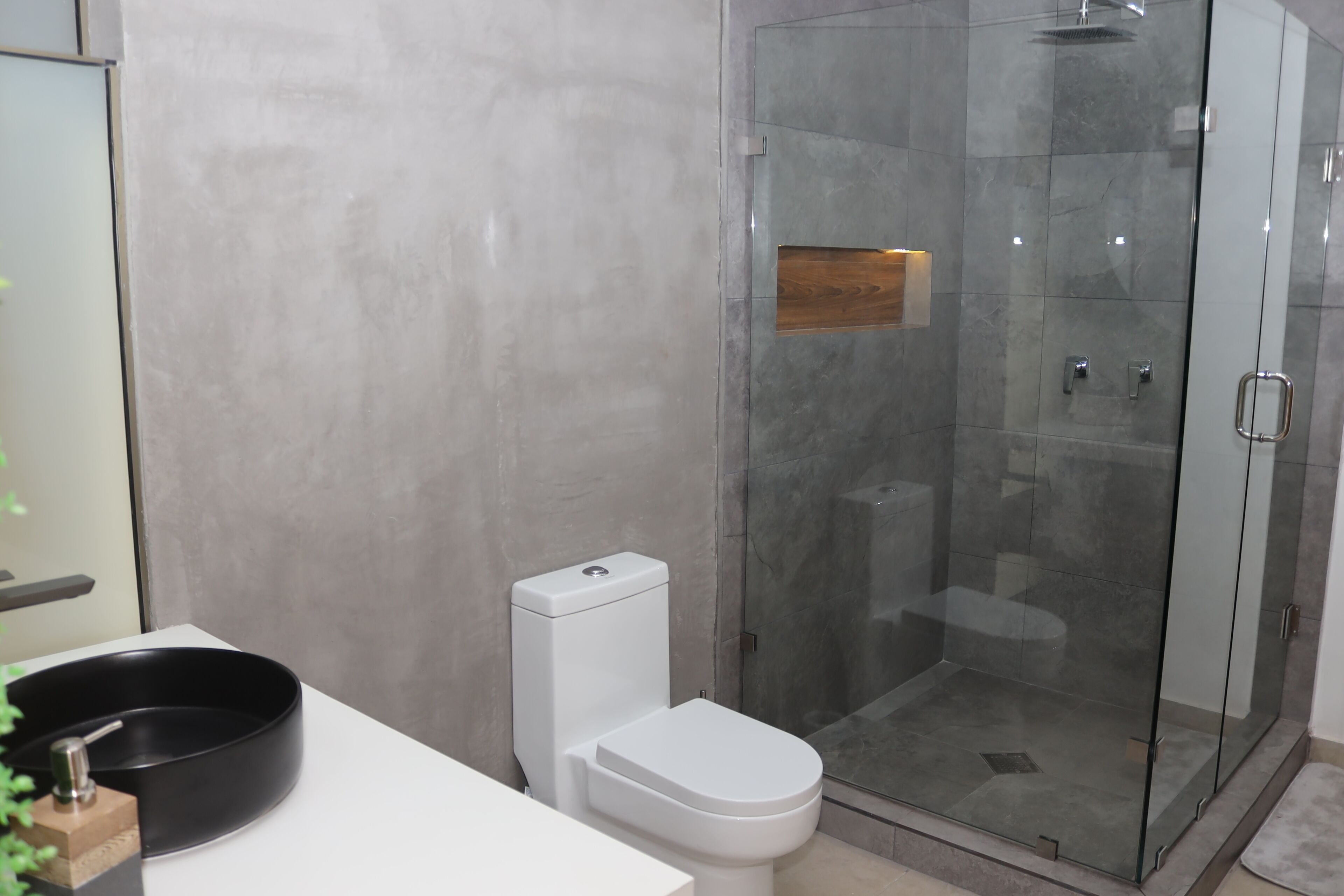 Een moderne badkamer met een glazen douchecabine, een wit toilet en een zwarte wastafel.