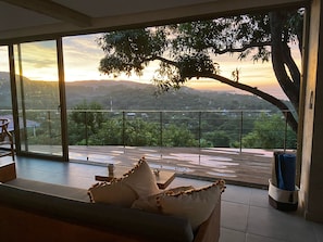 Ein Zimmer mit einer großen Glasschiebetür, die auf einen Balkon mit Blick auf einen Hügellandschaft im Sonnenuntergang führt.