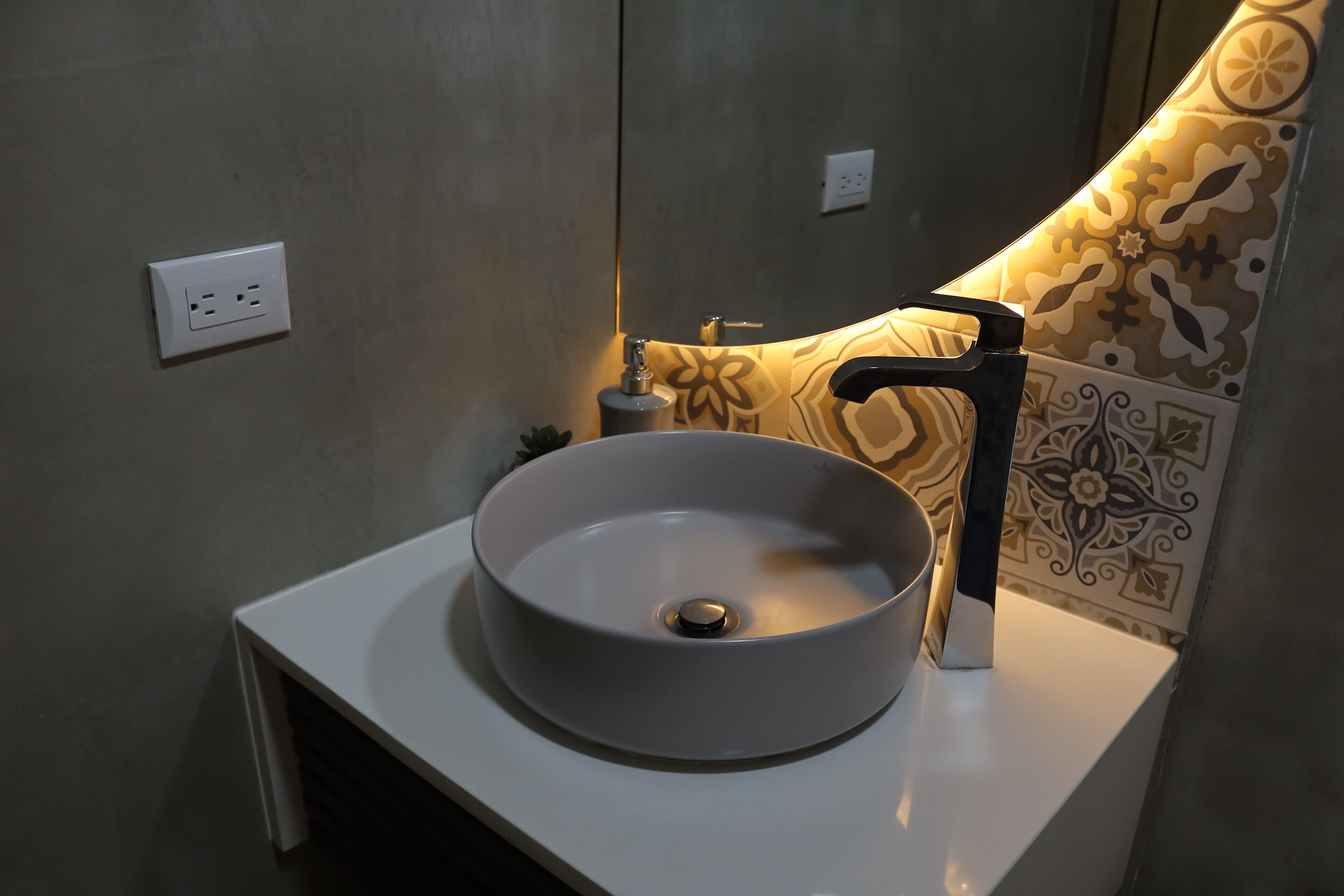 Une salle de bain avec un lavabo blanc, un robinet noir et des carreaux à motifs.