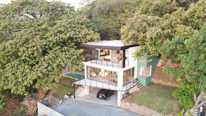 Une maison moderne à deux étages, dotée d’une façade en verre, avec une voiture garée dans l’allée et un jardin luxuriant qui entoure la propriété.