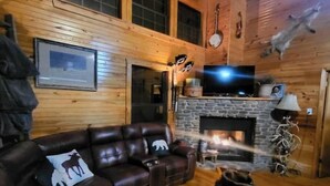 Un acogedor interior de cabaña con chimenea de piedra, sofá de cuero y televisión montada en la pared.