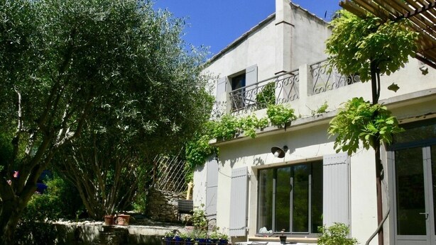 A two-story building with a balcony, a stone wall, and a garden area with a table and chairs.
