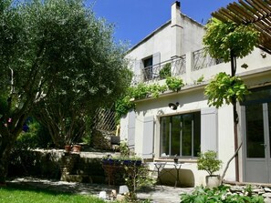 Un bâtiment à deux étages doté d’un balcon, d’un mur en pierre et d’un espace jardin avec une table et des chaises.