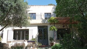 A two-story house with a balcony, a front door, and a small garden with potted plants.