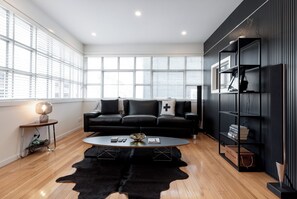 A modern living room with a black sofa, a coffee table, and a black leather rug. - Inner City Living Sum (Launceston)