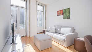 Un salon moderne avec un canapé, un pouf et un téléviseur à écran plat.
