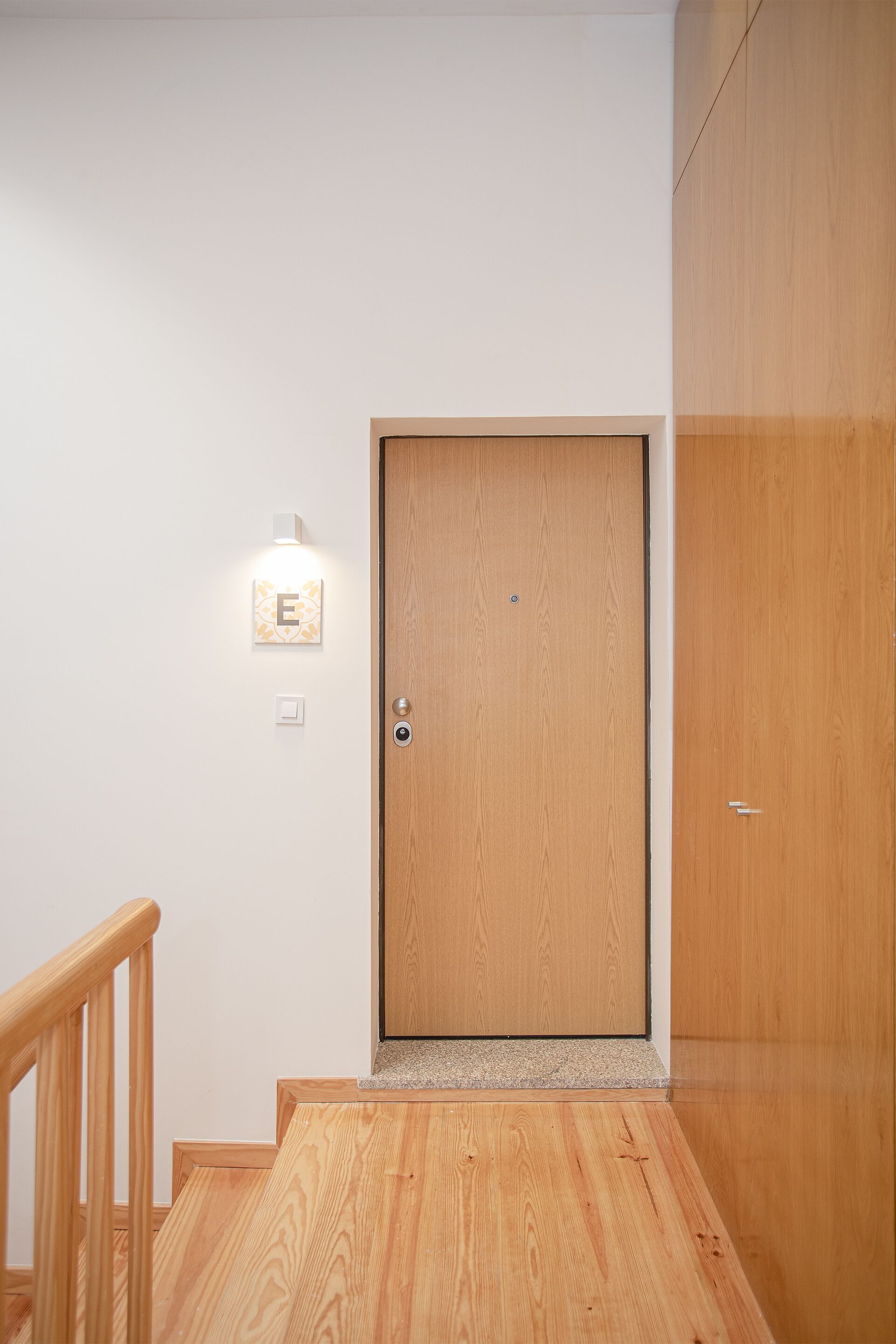 A wooden door with a light switch and a wall-mounted light fixture above it.