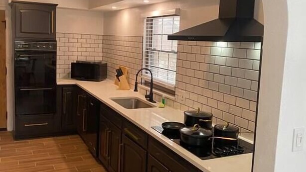 Une cuisine avec des meubles de couleur sombre, un plan de travail blanc, une cuisinière noire et une fenêtre donnant sur un beau paysage.