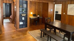 Un coin repas avec une table et des bancs en bois, un bureau avec une lampe et une étagère ornée d’objets décoratifs.