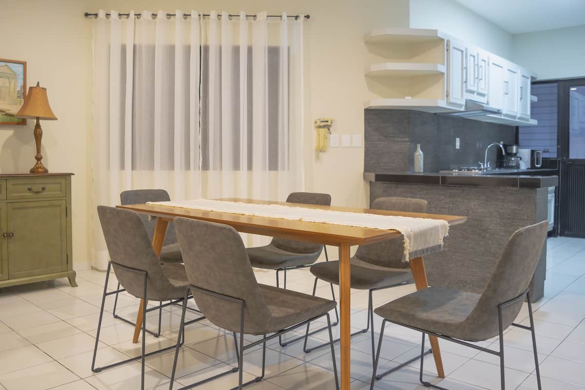 Un comedor con una mesa y sillas, una cocina con mostrador y armarios, y un ventanal con cortinas.