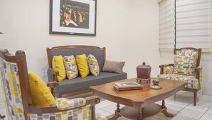 A living room with a sofa, armchair, and coffee table. There is a framed picture on the wall and a window with blinds. - Gaviotas Apartments (Mazatlán)
