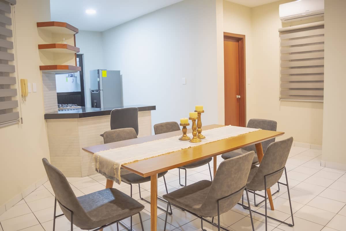 Un comedor con una mesa de madera, seis sillas y una cocina al fondo.