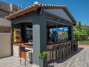 An outdoor bar area with a stone wall, a tiled roof, and a bar counter with stools. - Astarte Villas - Coco Palm Deluxe 3 Bedroom Suite (Ζακυνθος)