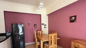Cocina compacta con zona de comedor, que incluye refrigerador, mesa de madera, sillas y una lámpara colgante.