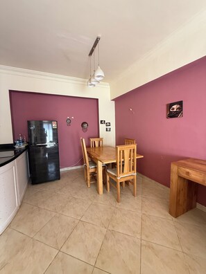 Una cucina compatta con zona pranzo, che include un frigorifero, tavolo in legno, sedie e una lampada a sospensione.