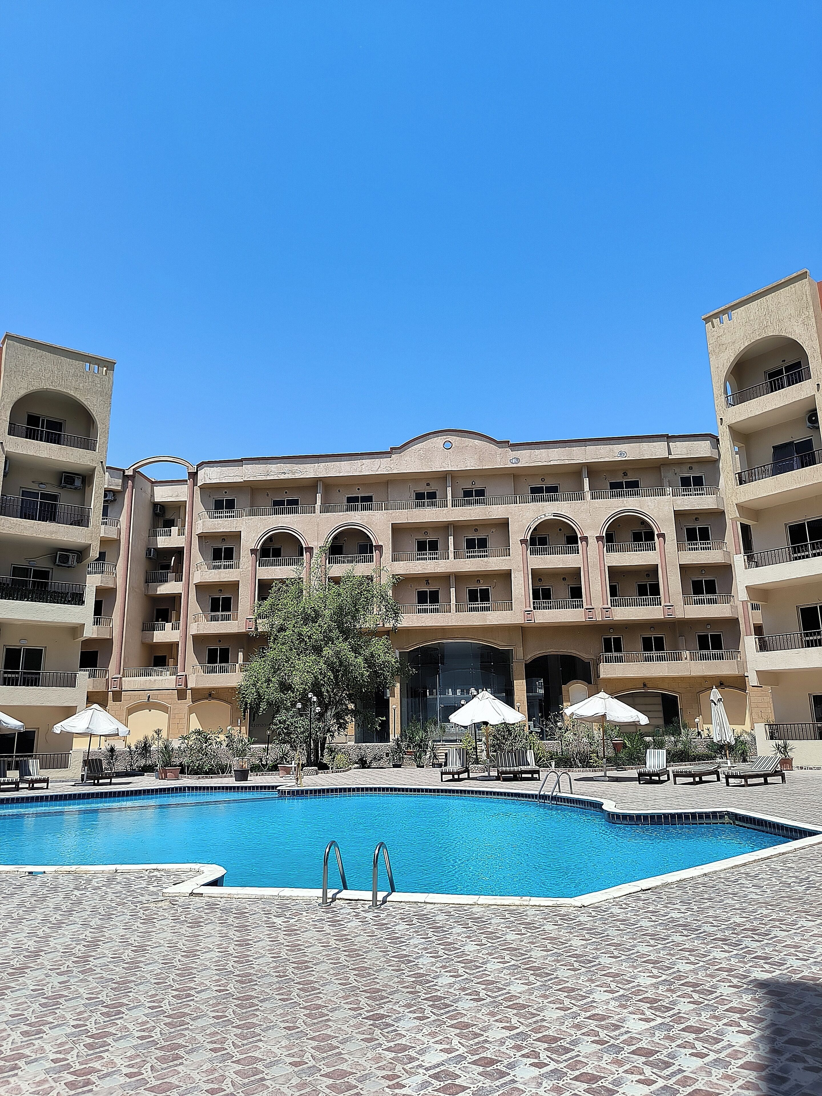 A hotel with a swimming pool, multiple balconies, and outdoor seating areas.