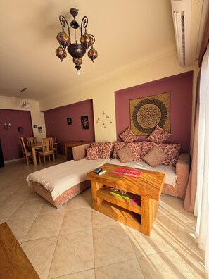 A living room with a sofa, a coffee table, a chandelier, and a wall with a decorative piece.