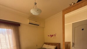 Un dormitorio con una cama, cabecera de madera, una lámpara en el techo, un equipo de aire acondicionado y una puerta.