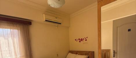 A bedroom with a bed, a wooden headboard, a ceiling light, an air conditioning unit, and a door.