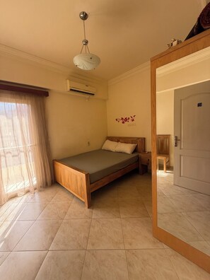 Una camera da letto con un letto, una testiera in legno, una lampada a soffitto, un condizionatore e una porta.