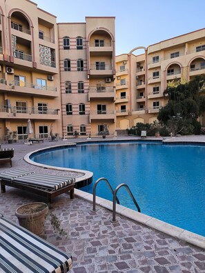 A swimming pool with lounge chairs and a stone-tiled deck. - Apartment in the center of Hurghada 7 min walk from the beach (Hurghada)