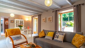 Una sala de estar con sofá, sillón y mesa de centro, un comedor con mesa y sillas, y vistas al exterior.