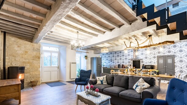 A modern living room with a stone wall, a fireplace, a sofa, and a dining area with a kitchen in the background. - Gite La Petite Ferme (Clermont-les-Fermes)