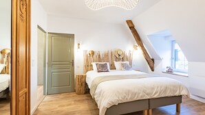A bedroom with a large bed, wooden headboard, a wooden wardrobe, a small bedside table, and a window with a view. - Gite La Petite Ferme (Clermont-les-Fermes)