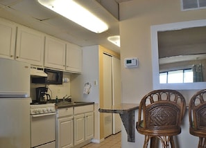 A kitchen with white cabinets, a microwave, a stove, and a window with blinds.