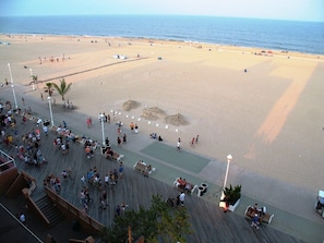 A beach with a boardwalk, people, and beach umbrellas.