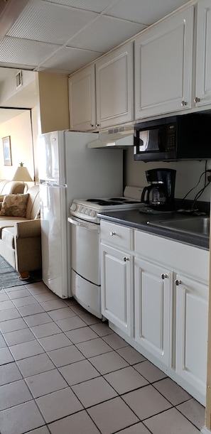 A compact kitchen with white cabinets, a stove, a microwave, and a refrigerator.