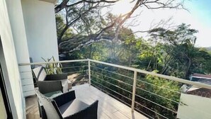 A balcony with a chair and a small table, overlooking a garden with trees and a fence. - Deluxe Penhouse with Pool - 3 min walk to the beach (Playa Pelada)