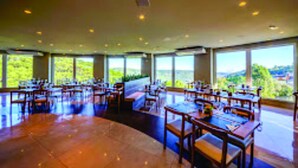 Un'ampia sala da pranzo con numerosi tavoli e sedie, e grandi finestre che si affacciano sul verde circostante.
