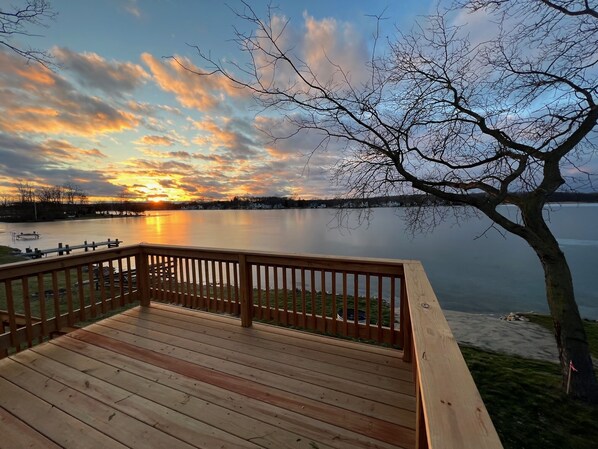 Una terraza de madera con vistas a un lago tranquilo, con un atardecer de fondo.