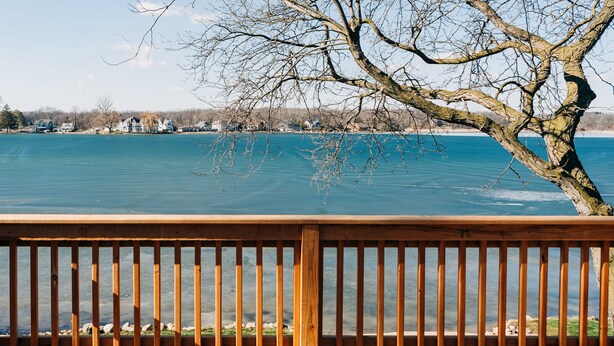A wooden deck with a view of a lake and houses in the background. - Steps from the water, Sandy beach - ahhh… (Brighton)