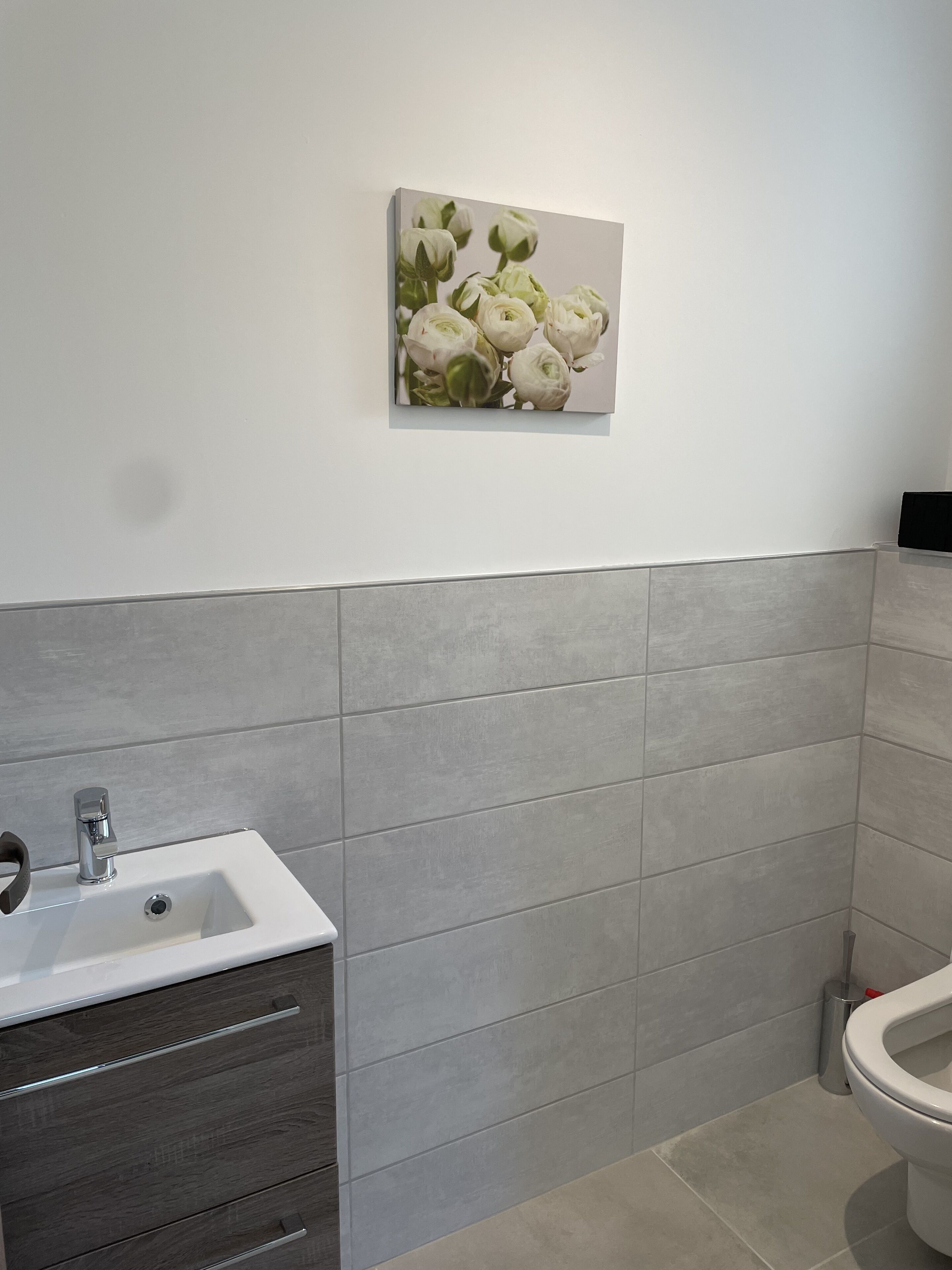 Un baño con un lavamanos blanco, cajones de madera oscura, baldosas grises y un inodoro.