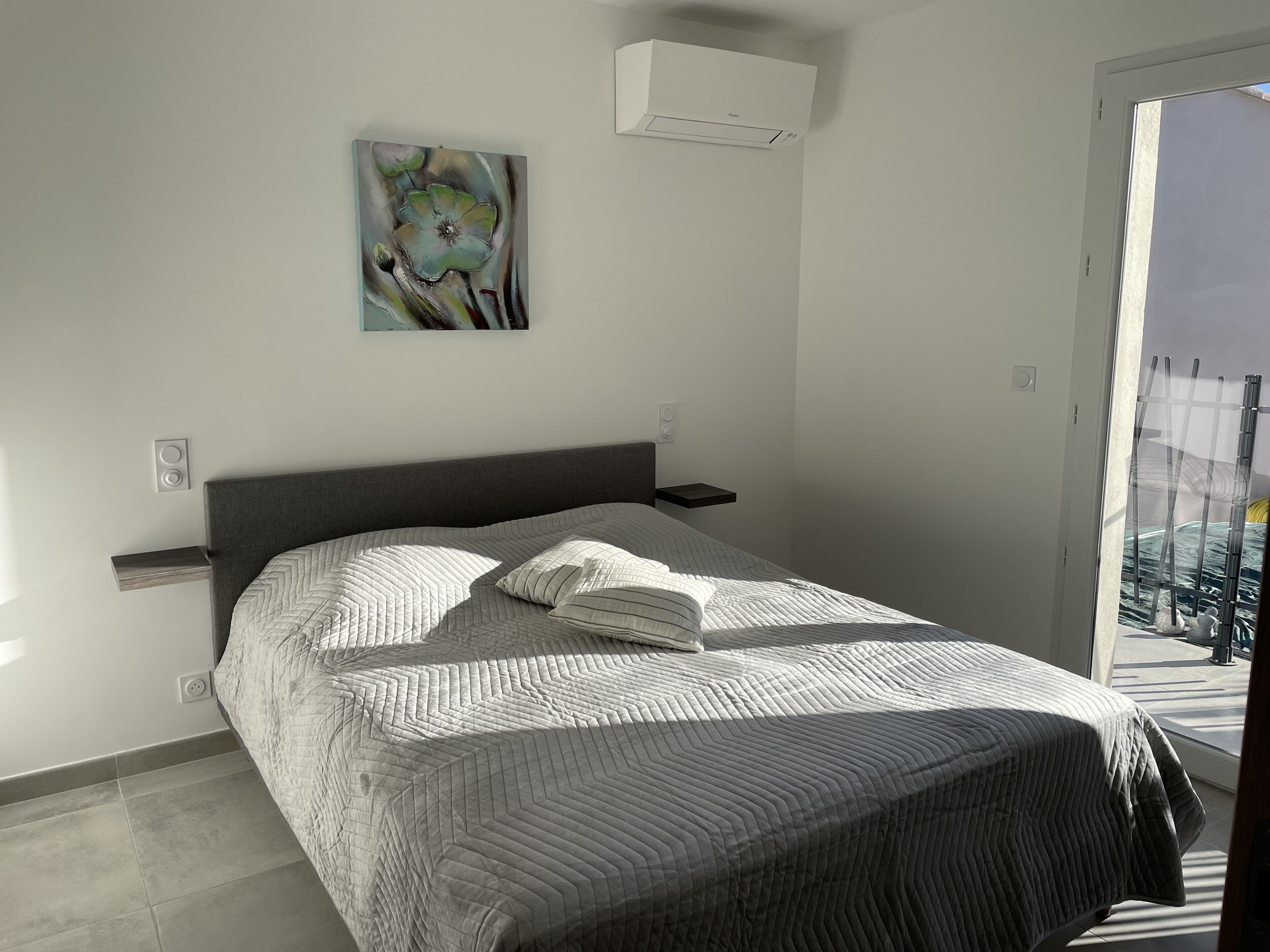 Een slaapkamer met een bed, een nachtkastje, een wandairconditioner en een schilderij.