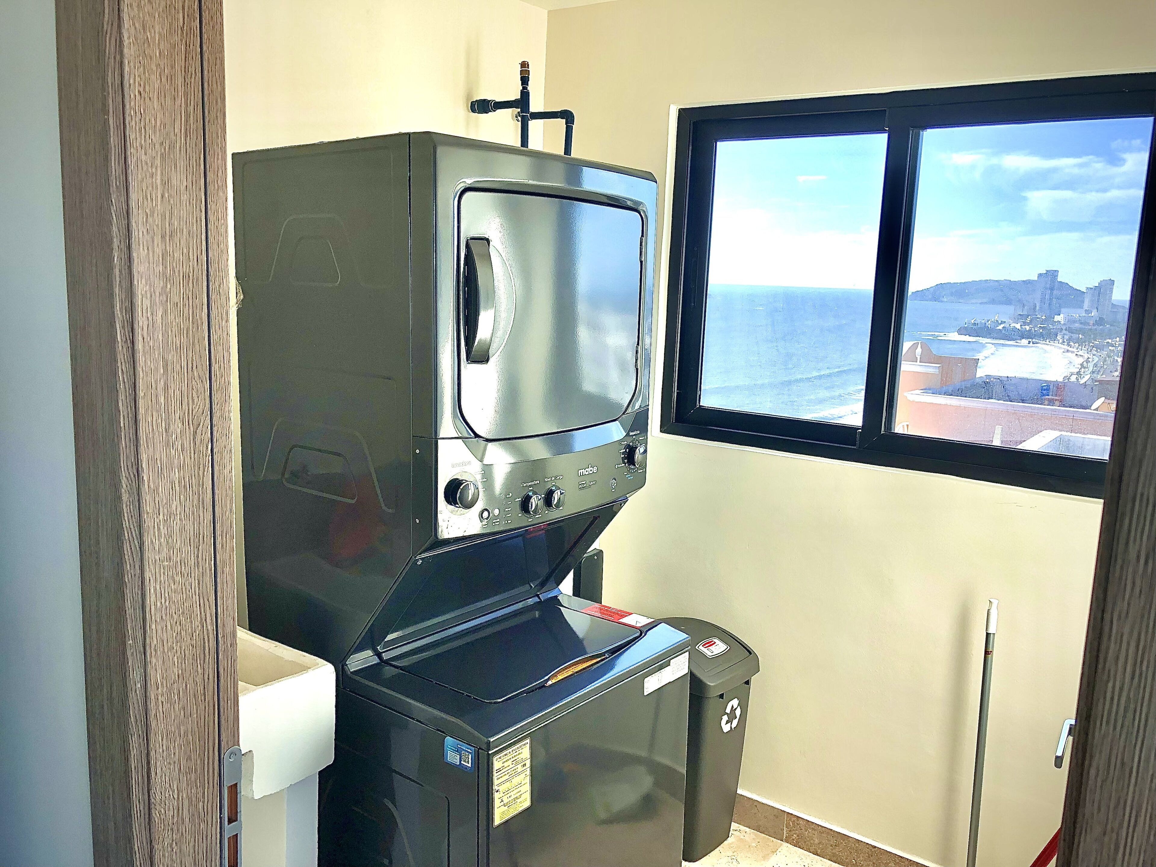 A compact kitchenette with a built-in microwave, a small trash bin, and a window offering a view of the sea and cityscape.
