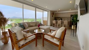 Una sala de estar moderna con un sofá, sillas, una mesita y una cocina al fondo.