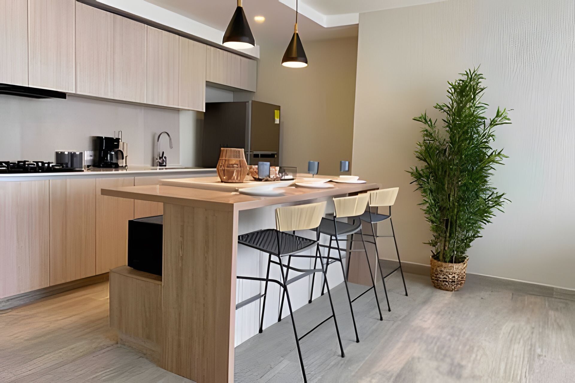 A modern kitchen with a central island, bar stools, a potted plant, and a pendant light.