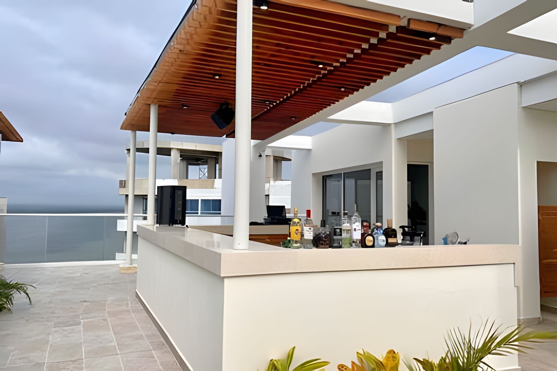 Een modern buitengebied met een bar, een houten pergola, een zwembad en uitzicht op zee.