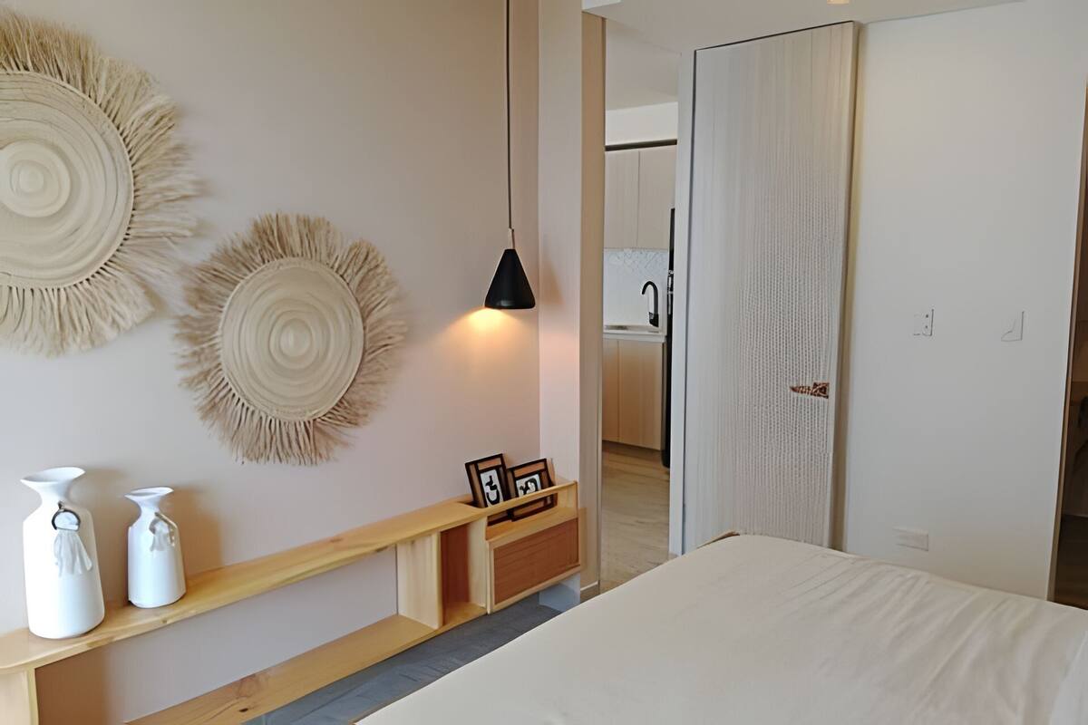 A bedroom with a bed, a bedside table with decorative items, a hanging light fixture, and a wardrobe.
