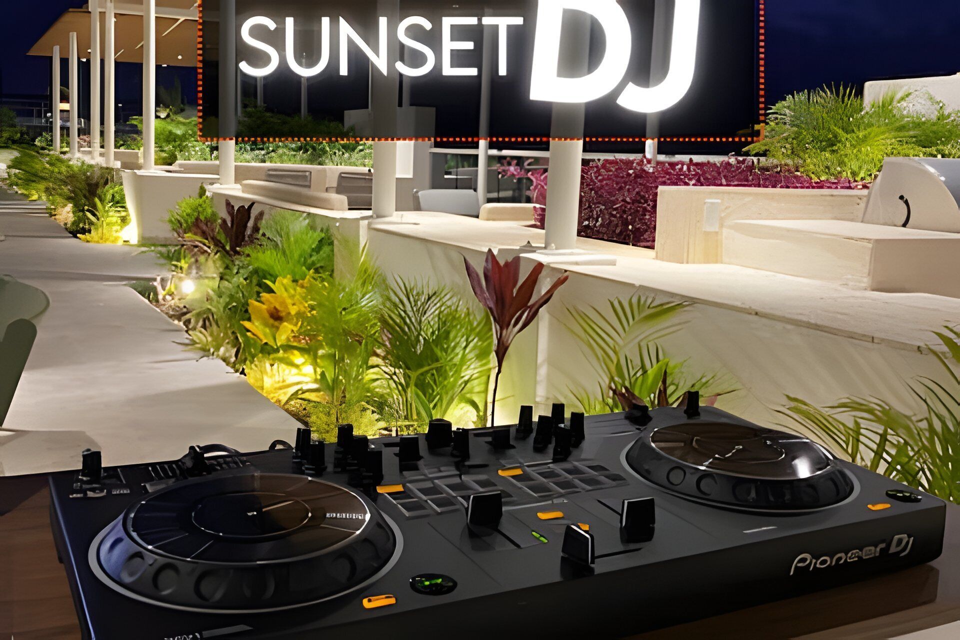 Equipo de tocadiscos Pioneer para DJ al aire libre con un cartel que dice 'SUNSET DJ' al fondo.