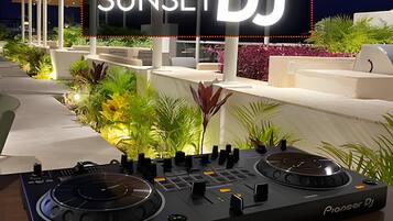 Equipo de tocadiscos Pioneer para DJ al aire libre con un cartel que dice 'SUNSET DJ' al fondo.