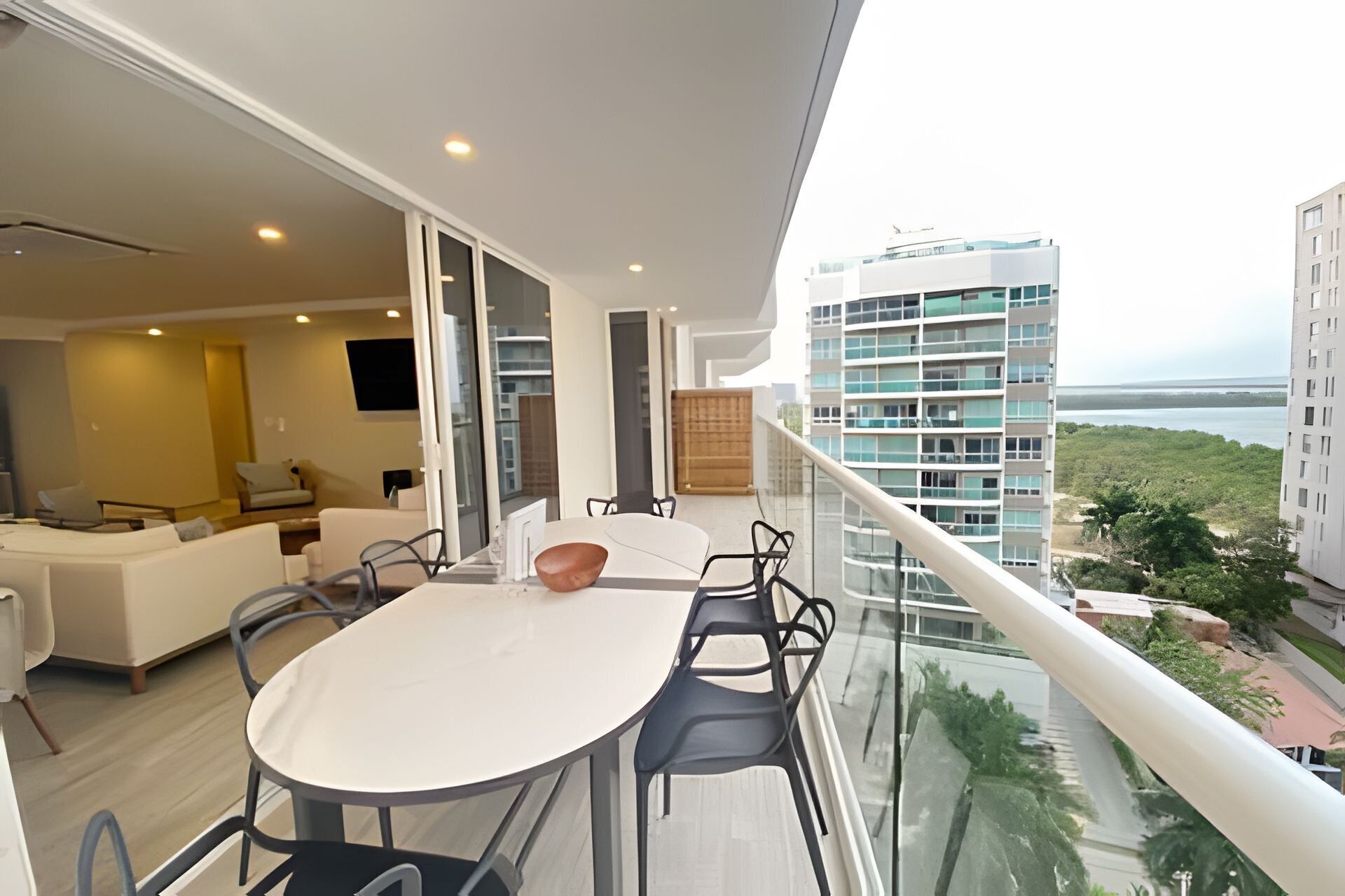 A balcony with a dining table and chairs, a sofa, and a television in a modern living room.