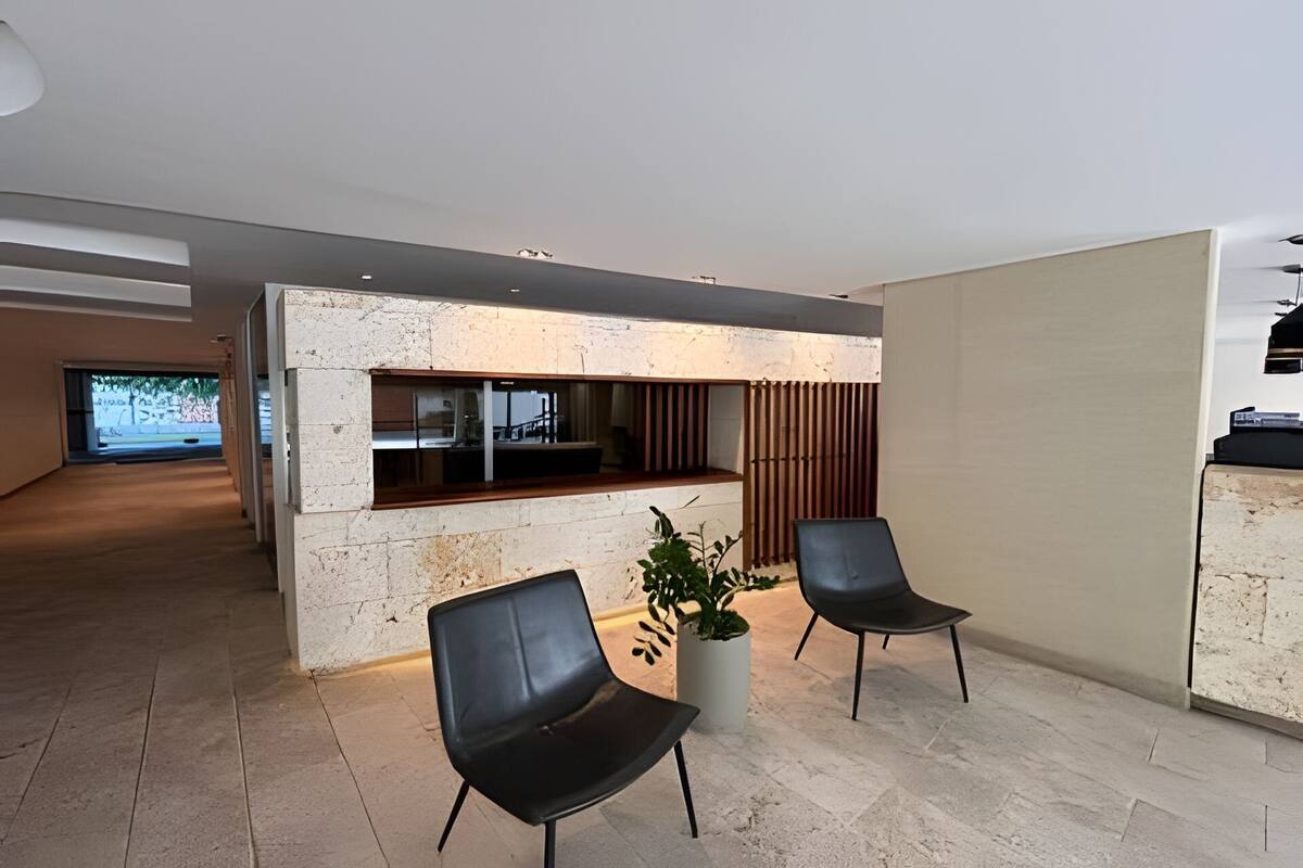 A modern lobby with a reception desk, two black chairs, a potted plant, and a large TV screen.